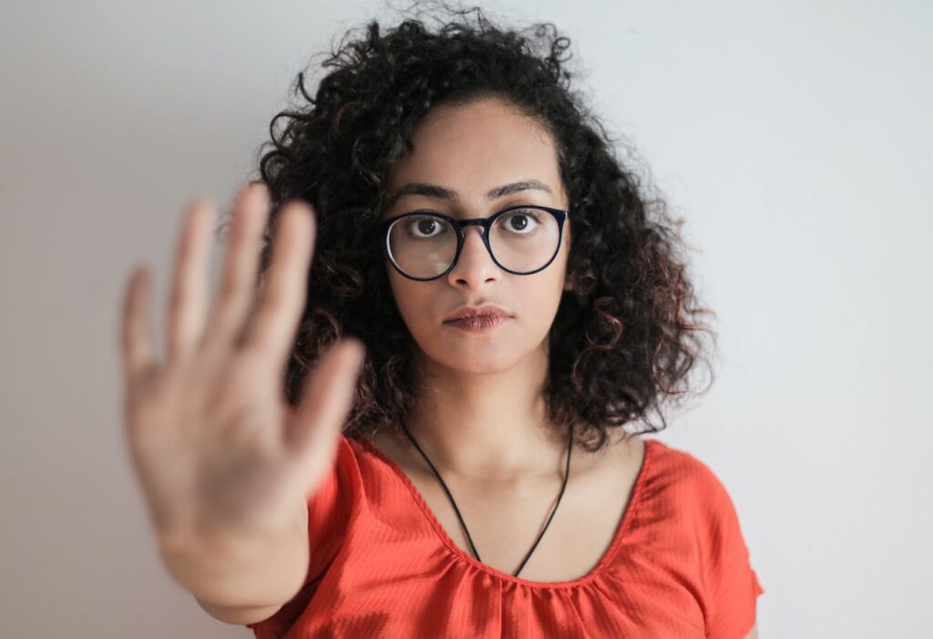 portrait photo of woman in red top wearing black framed eyeglasses holding out her hand in stop gesture