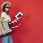 happy female traveler with suitcase on red background