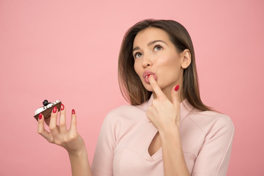 woman eating cupcake while standing near pink background inside room
