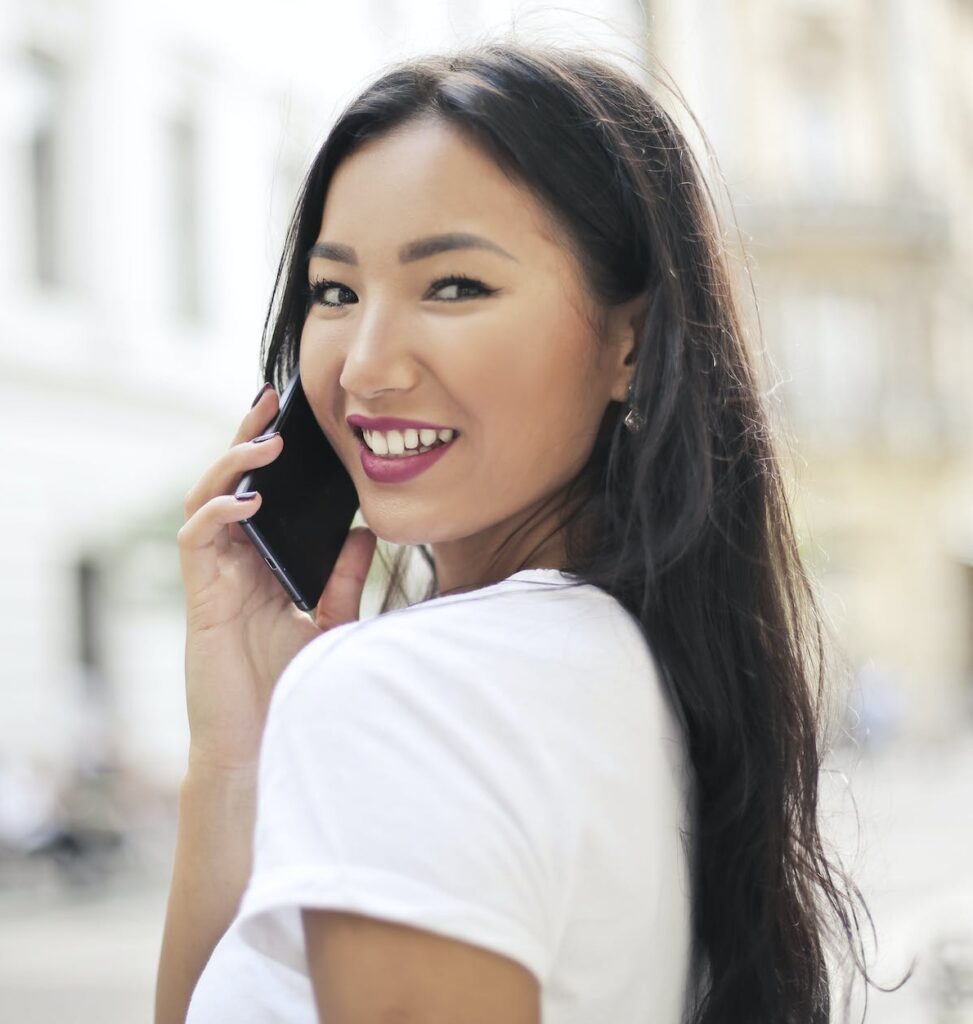 selective focus photo of smiling woman in white t shirt talking on the phone