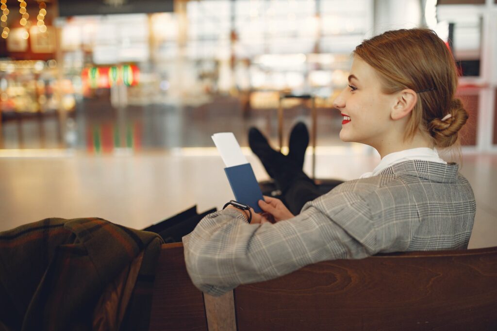 happy young woman waiting for flight and relaxing in waiting area of airport