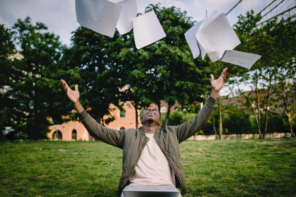 excited male student throwing university papers in air