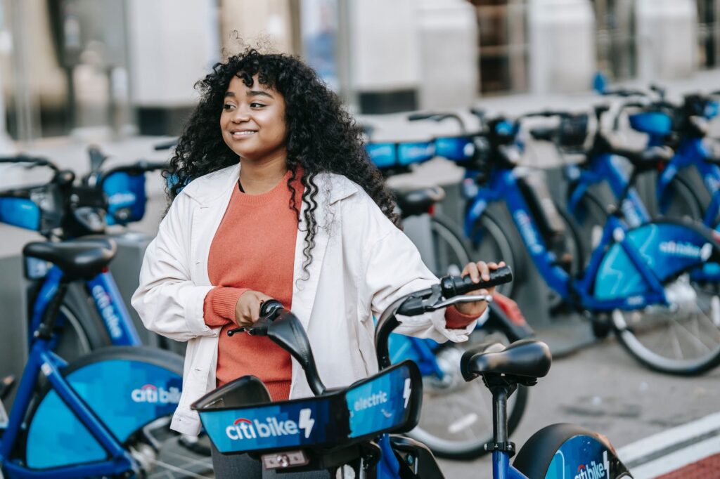 smiling black woman walking with bicycle along street renting station