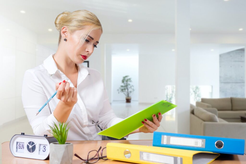 blond woman wearing a white shirt checking standing by a desk with folders
