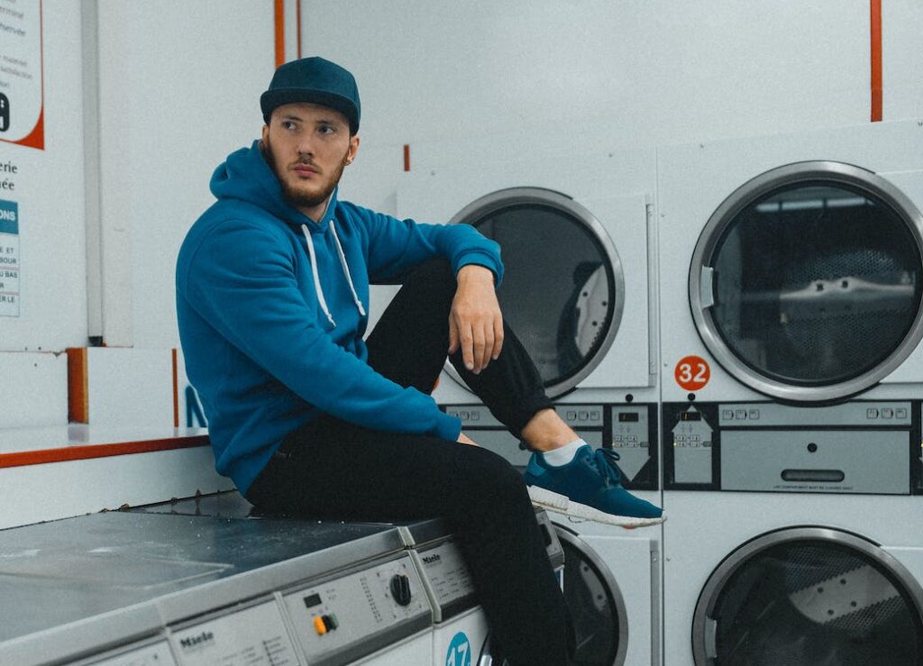 man sitting on top of washing machine in coin laundry