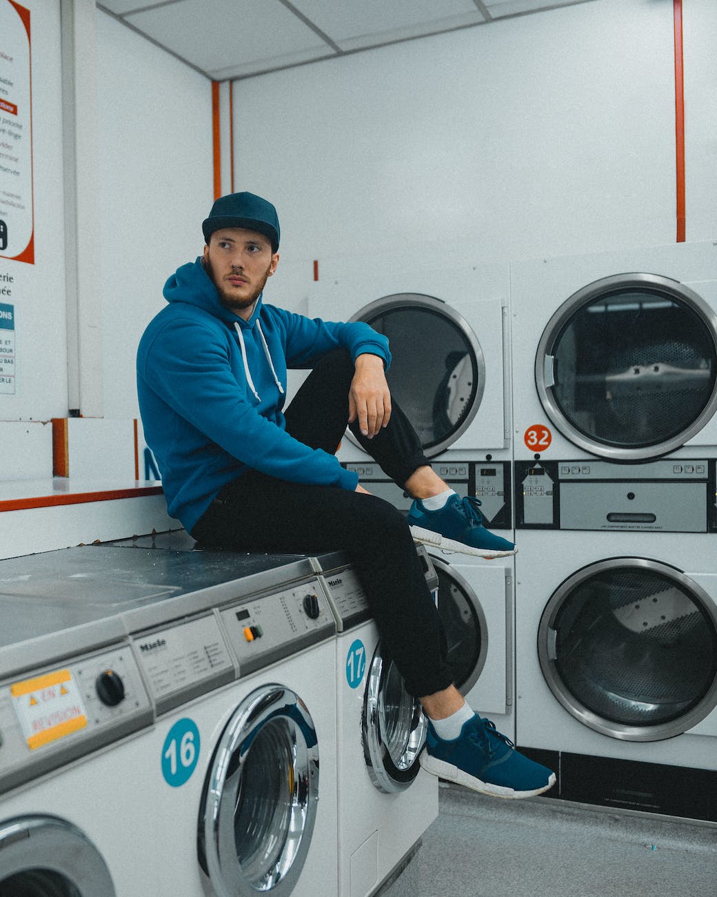 man sitting on top of washing machine in coin laundry