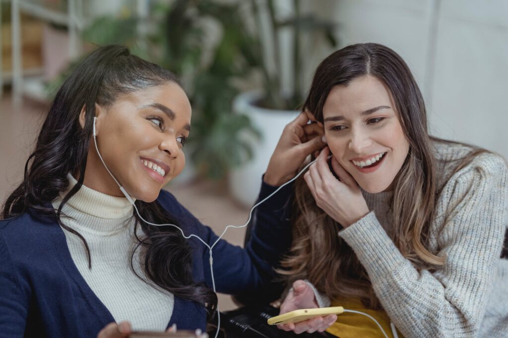 delighted young multiethnic female friends smiling and listening to music in earphones