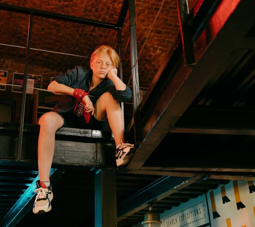 woman in red t shirt and blue denim jeans sitting on brown wooden ladder