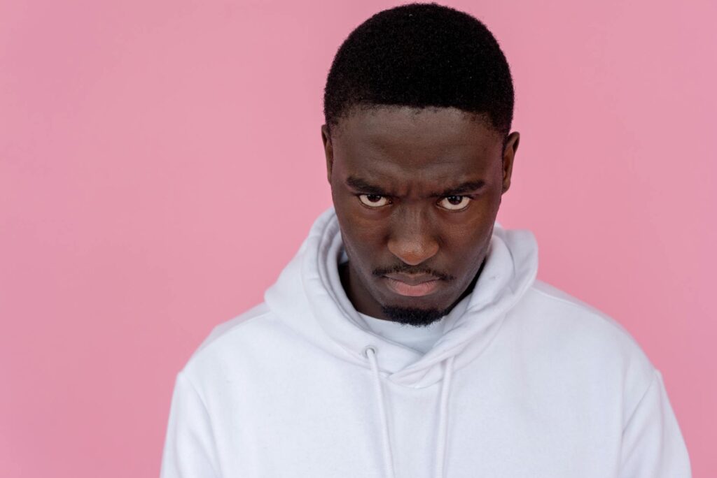 angry black man in hoodie against light pink background