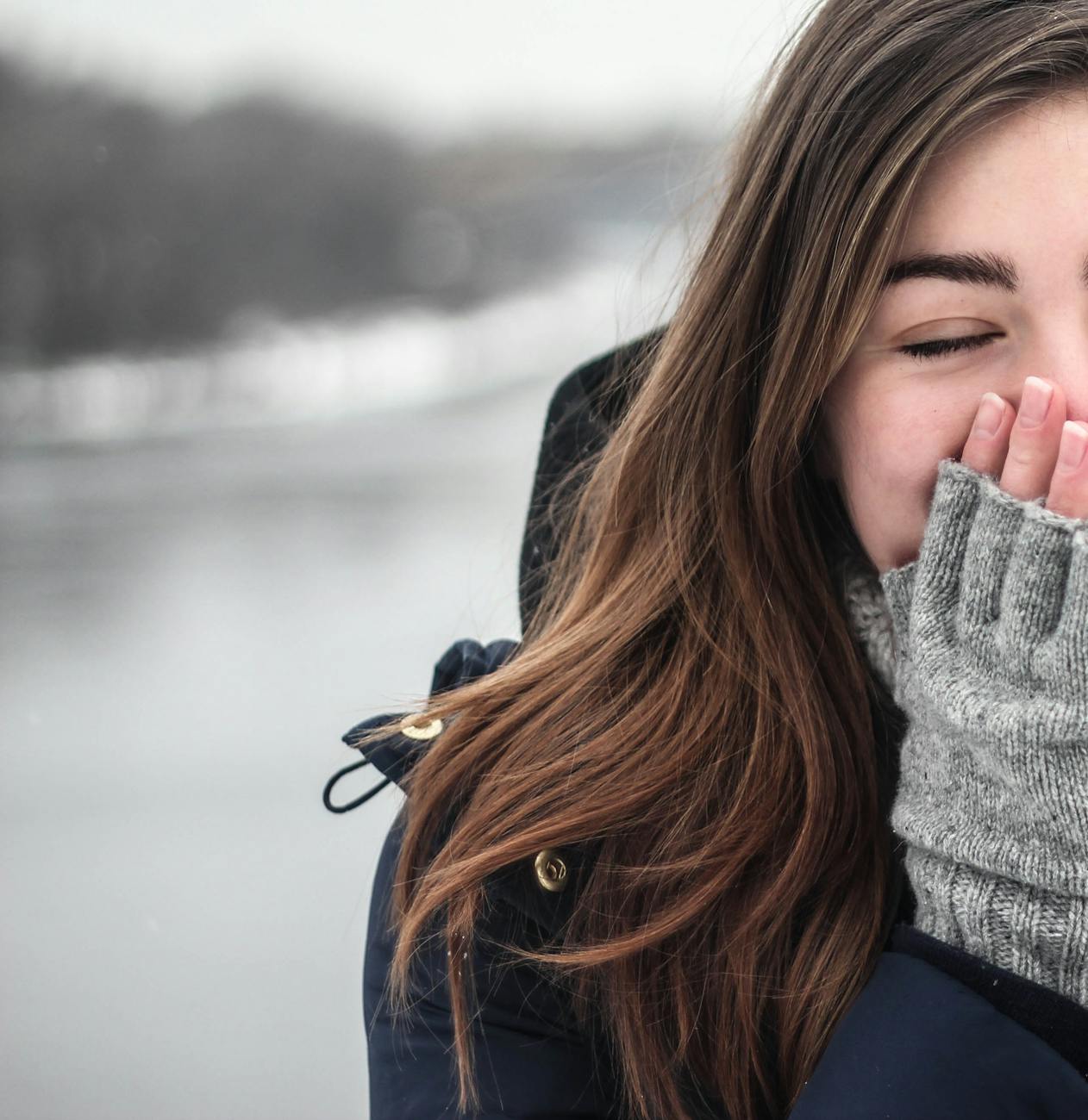 woman in black hooded down jacket covering her face with grey fingerless gloves