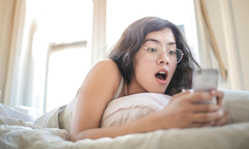 woman lying on bed holding smartphone