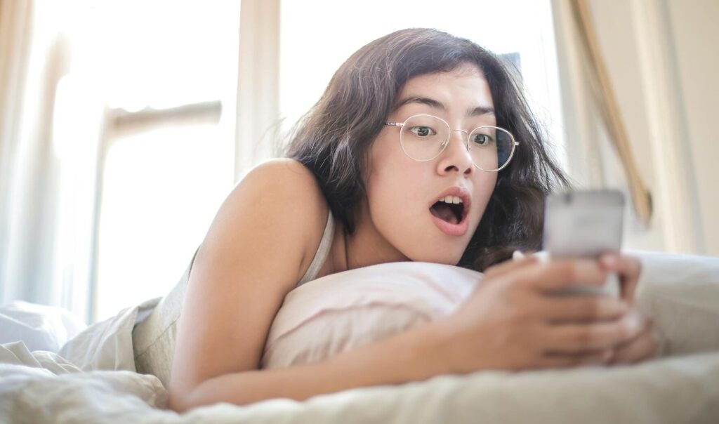 woman lying on bed holding smartphone