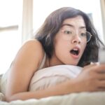 woman lying on bed holding smartphone